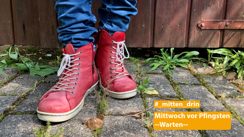 Füße mit roten Schnürschuhen vor stehen auf dem Pfalstersteinen und vor einer Holzwand