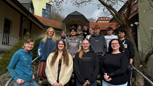 Es sind verschiedene Menschen auf der Treppe stehend unter einem Baum vor dem Jugendhaus in Roßbach zu sehen