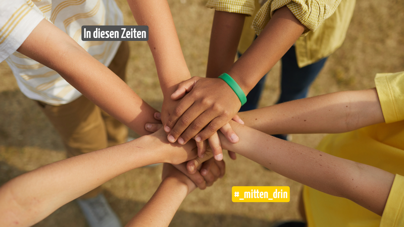 Vier Menschen stapeln ihre Hände in der Mitte übereinander.