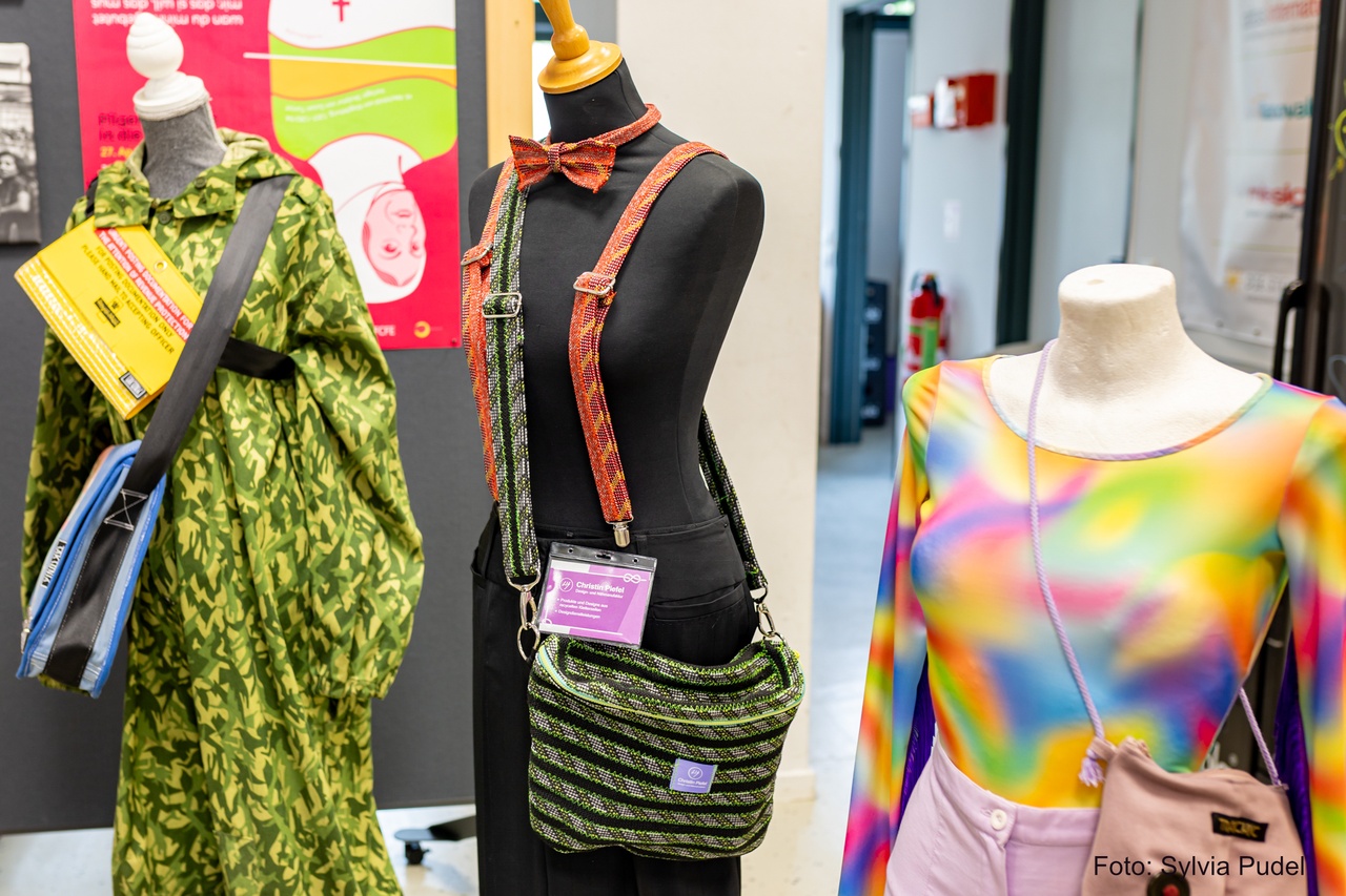 Es stehen drei Modepuppen nebeneinander. Diese tragen selbstgenähte Kleidung und Accessoires. Links in Camouflage. Mitte: Accessoires aus Kletterseil. Rechts: Regenbogenfarbener Sportbody.