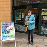 Mann spielt Saxophone vor einer offenen Tür. Neben ihn steht ein Aufsteller mit einem Plakat zur Fashon Revolution Week Magdeburg.
