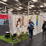 Ein Messestand mit Menschen die dort im Gespräch miteinander sind.