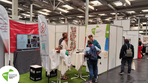 Ein Messestand mit Menschen die dort im Gespräch miteinander sind.