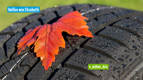 Bildbeschreibung: Man sieht die Oberseite eines Autoreifens, auf dem Wassertropfen haften. Oben drauf liegt ein großes, vom Herbst rot verfärbtes Ahornblatt.