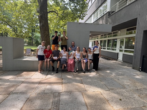 Es ist eine Gruppe Jugendliche zu sehen, die sich unter Bäumen vor einem Haus zu einem Gruppenfote aufgestellt haben