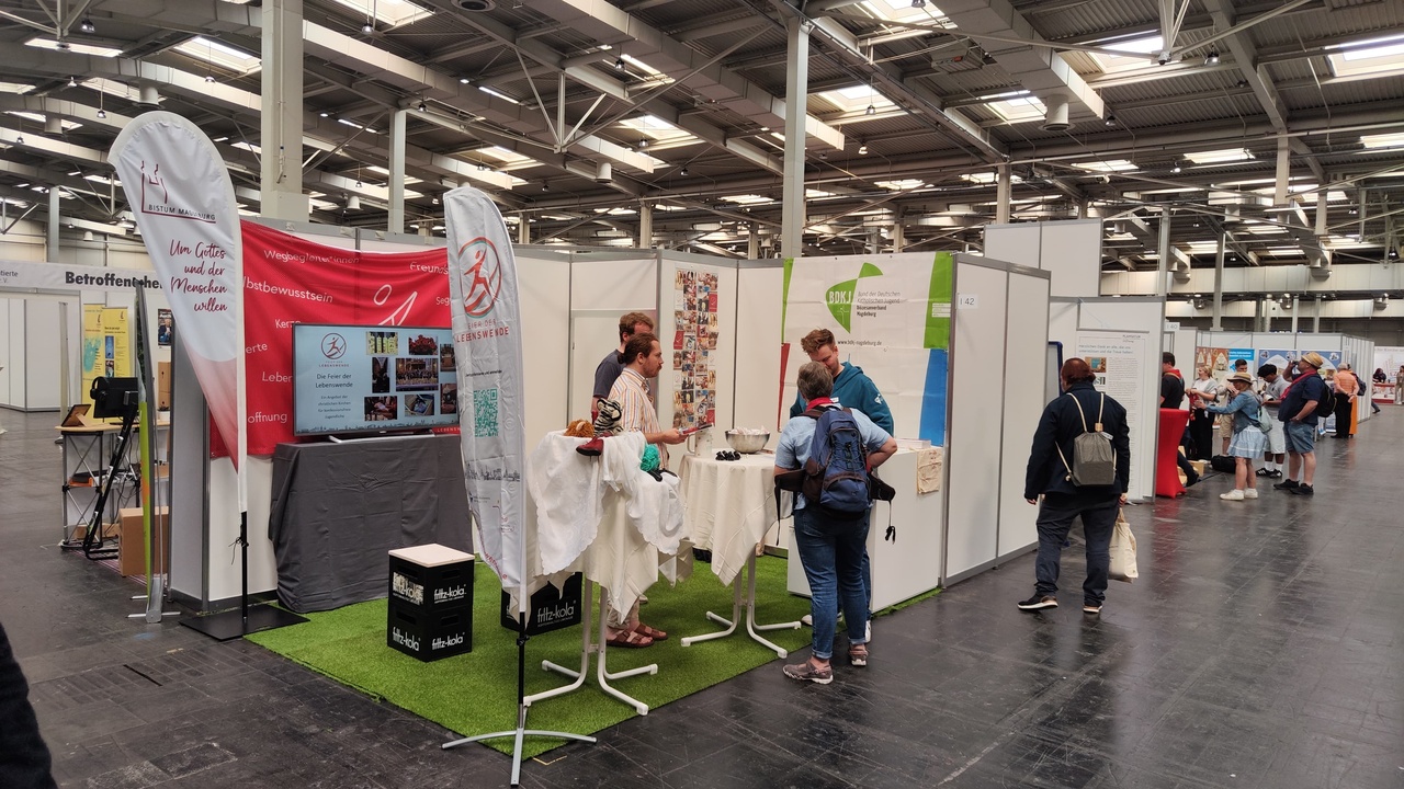 Ein Messestand mit Menschen die dort im Gespräch miteinander sind.