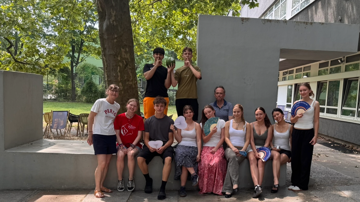 Es ist eine Gruppe Jugendliche zu sehen, die sich unter Bäumen vor einem Haus zu einem Gruppenfote aufgestellt haben